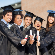 Portrait of happy students in graduation gowns showing diplomas on university campus