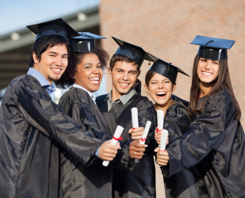 Portrait of happy students in graduation gowns showing diplomas on university campus
