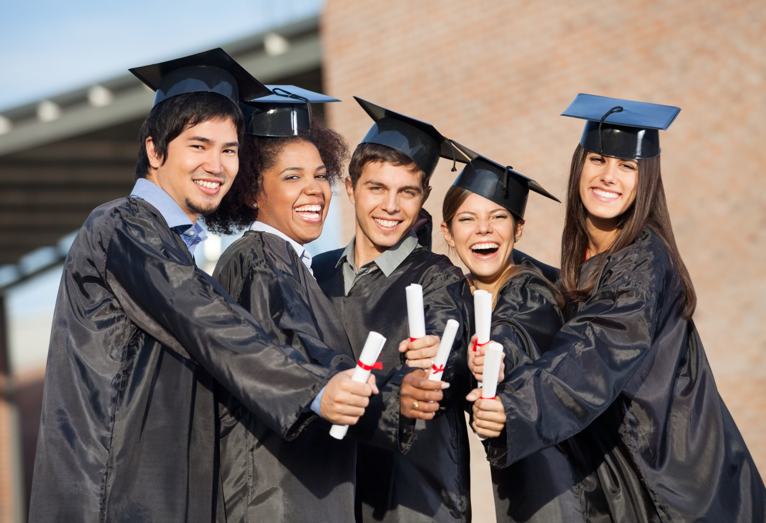 Portrait of happy students in graduation gowns showing diplomas on university campus