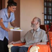 nurse or helper in residential home giving food to senior man