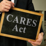 a man holds a small chalkboard with the words CARES Act on it
