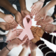 a circle of hands of all races holding a pink breast cancer ribbon in the middle