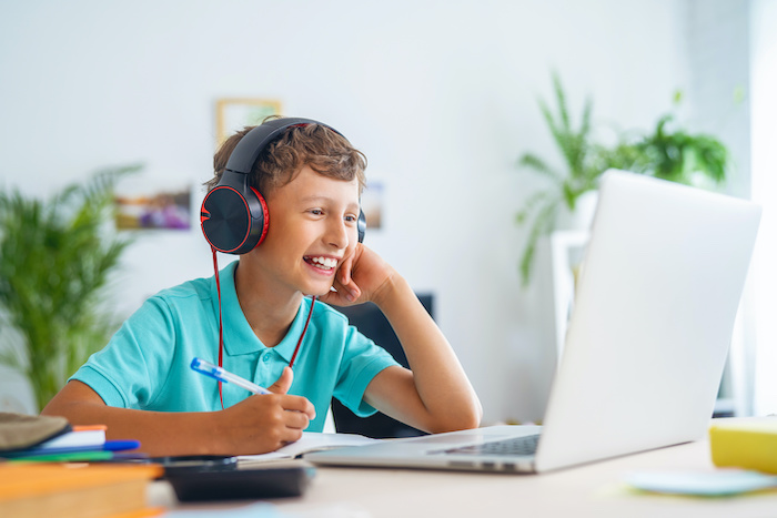 cheerful boy with headphones uses laptop for online school