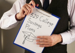 529 College Savings Plans is shown written on a page on a clipboard held by the hands of a person whose face is not in the frame