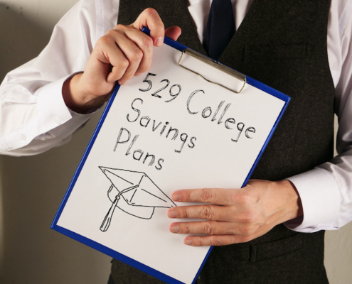 529 College Savings Plans is shown written on a page on a clipboard held by the hands of a person whose face is not in the frame