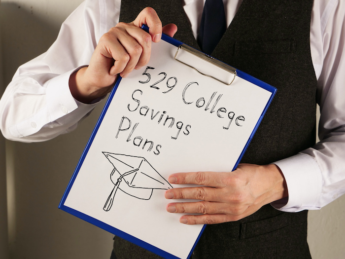 529 College Savings Plans is shown written on a page on a clipboard held by the hands of a person whose face is not in the frame