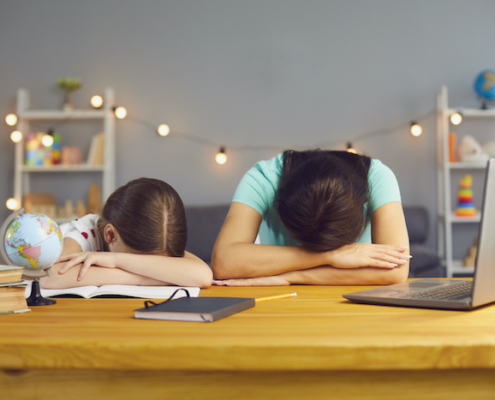 Little girl with her mother lying on table near laptop computer, exhausted from online home schooling