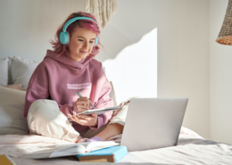 Hipster teen girl student with pink hair watch online webinar learning in bed.