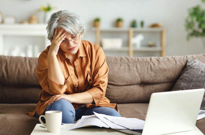 stressed woman with hand to forehead looking at financial papers and computer