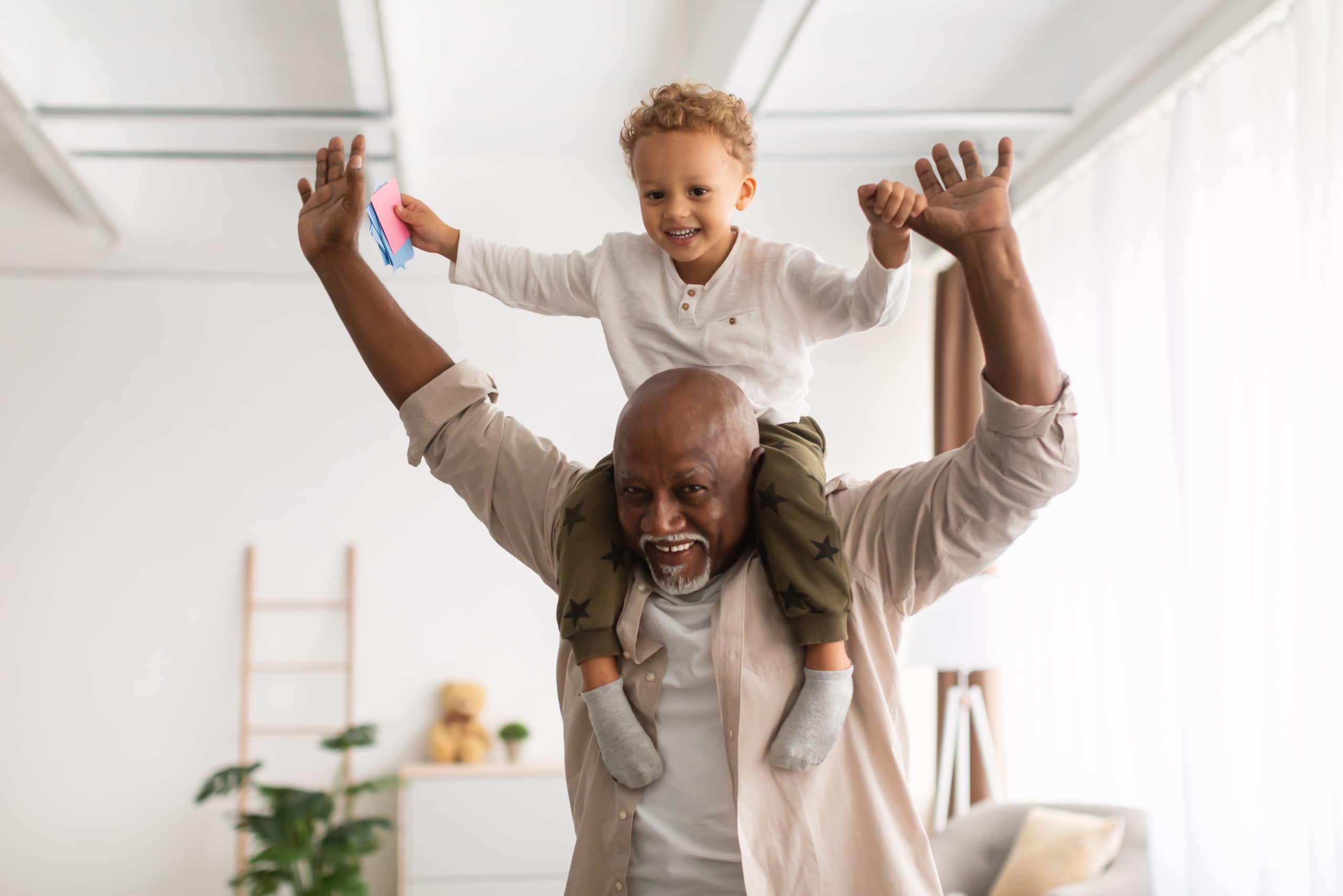 Cheerful African American man carrying his grandson on his shoulders while playing indoors. Federal employees can take advantage of phased retirement to ease the transition from full-time work to leaving the workforce.