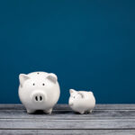 A small white piggy bank looking at a larger white piggy bank