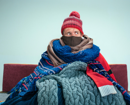 Bearded Man bundled in many scarves and blankets Sitting on Sofa at Home.