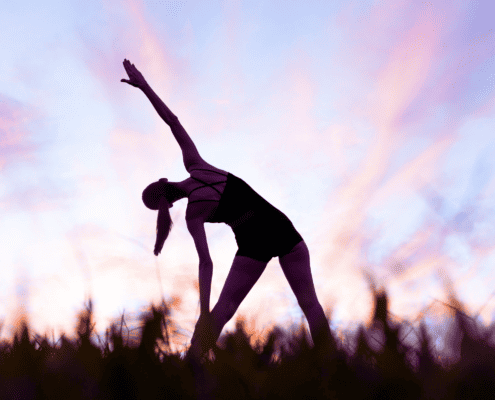 A silhouette of a woman with a sunrise sky demonstrates the Trikonasana, a standing yoga pose that opens the chest and shoulders, as well as providing a deep stretch for the hamstrings, groins and hips.