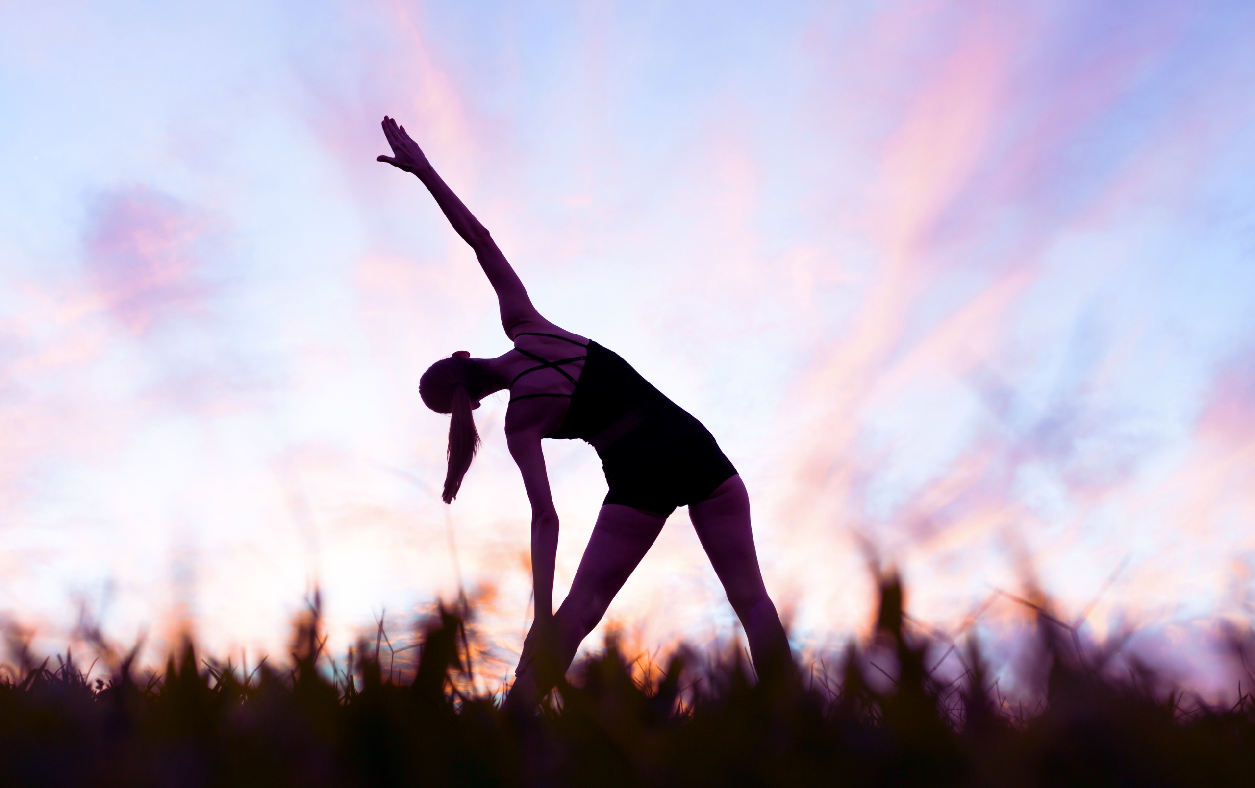 A silhouette of a woman with a sunrise sky demonstrates the Trikonasana, a standing yoga pose that opens the chest and shoulders, as well as providing a deep stretch for the hamstrings, groins and hips.