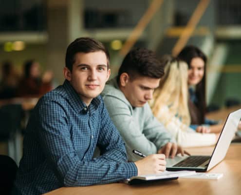 A caucasion college student smiling at the camera taking a break from working on his college scholarship applications. There are many resources, like our scholarship webinar, that can guide you through the process.