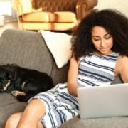 An African American woman sits on the couch next to her dog as she reads through applications as a virtual volunteer of the scholarship selection committee