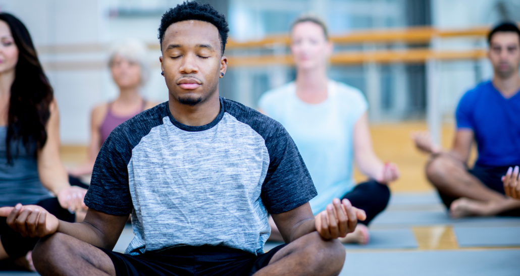 A Black man meditates as part of his self-care when stressed out.