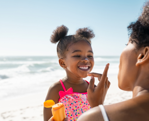 Protecting all members of your family from UV rays is critical. In this picture, a mother applying sunscreen on girl's face as outline during UV Safety Month