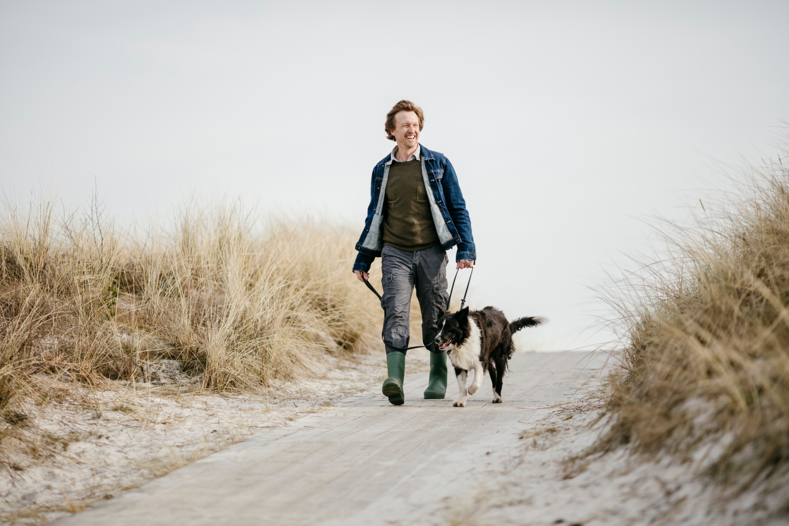 Practicing many elements of everyday self-care to maximize wellness, a man taking his border collie dog for a walk on the beach as a way to incorporate self-care