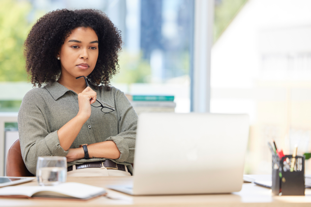 A woman contemplates her Federal Career Growth opportunities while sitting at her laptop with her arms folded and glasses to her chin.