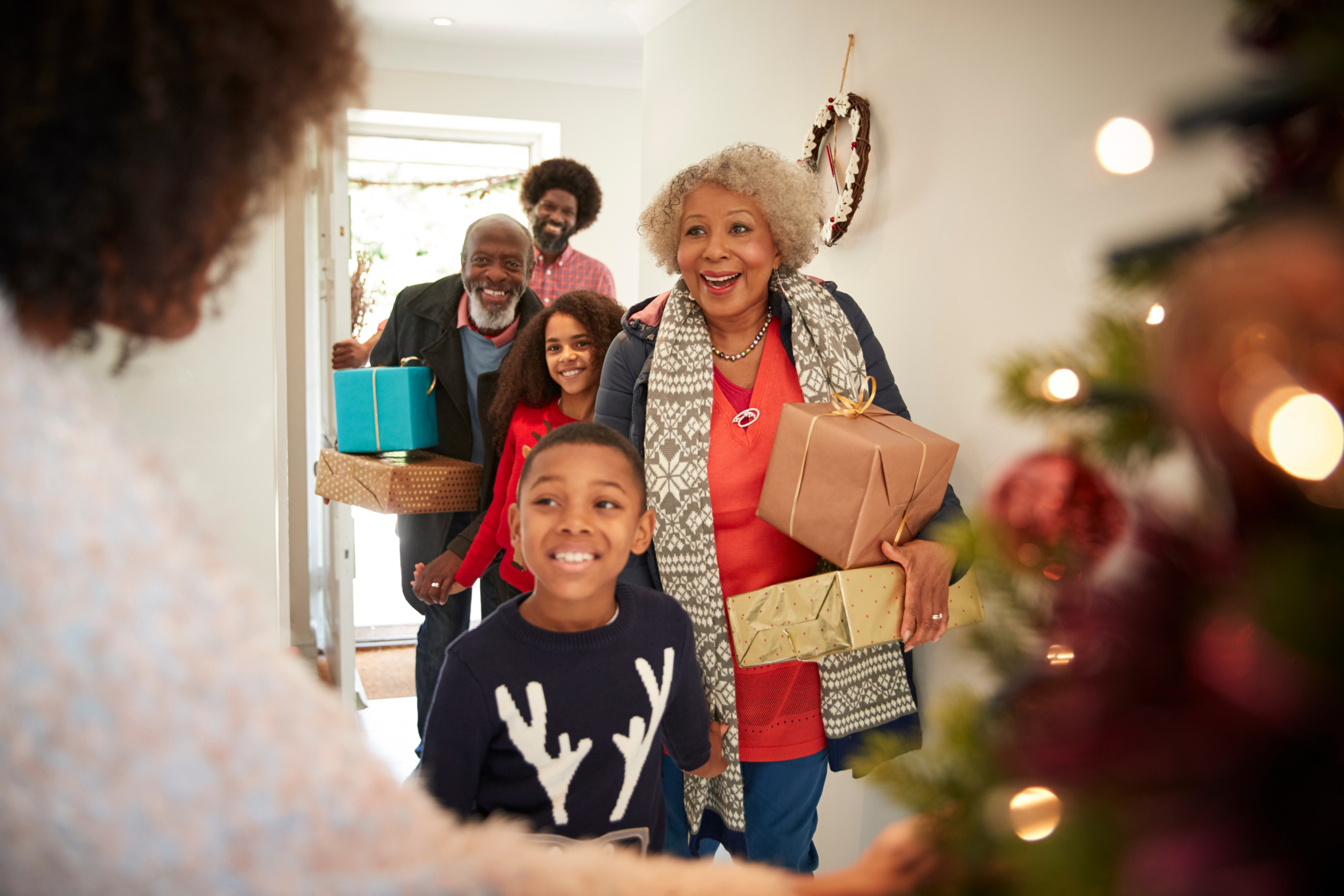 A family walks in the front door during the holiday season bearing gifts. Holiday budgeting tips with effective holiday financial planning can help keep your spending in line this season.