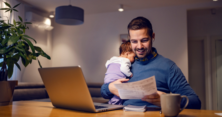 A man holds a sleeping baby while he reviews personal documents at home. Getting ahead on your finances for feds can set you and your family up for success