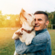 Happy young man holding dog Labrador in hands at sunset outdoors. Fireworks and pets are no match, so we take this opportunity to review 4th of July Pet Safety.