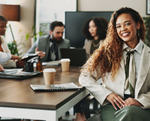 A woman smiles as coworkers collaborate in the background of a conference room. Strong teams and culture, clear expectations, and a healthy work life balance can lead to reduced workplace stress and workplace anxiety for federal employees.