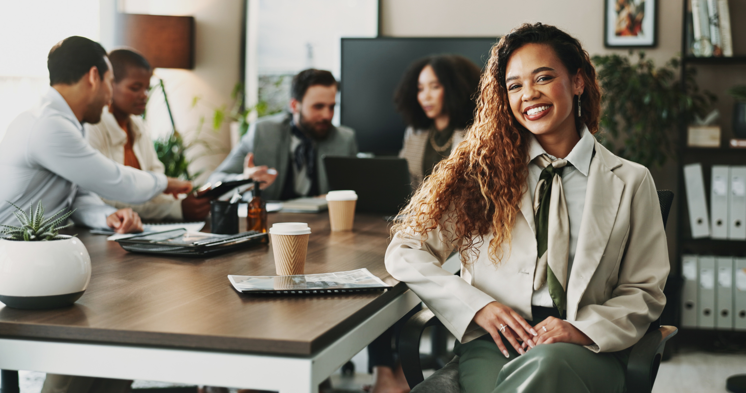 A woman smiles as coworkers collaborate in the background of a conference room. Strong teams and culture, clear expectations, and a healthy work life balance can lead to reduced workplace stress and workplace anxiety for federal employees.