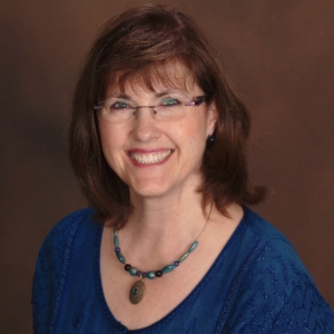 Kelly Reyes, a smiling white woman with brown hair and blue eyes, wearing glasses